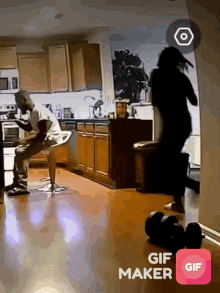 a man sits on a bar stool in a kitchen while a woman jumps in the air
