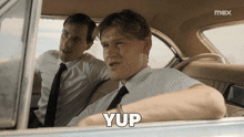 two men in suits and ties are sitting in a car with the word yup written in white