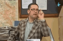 a man in a plaid jacket is talking on a cell phone while sitting at a desk .