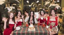a group of women dressed in santa outfits are sitting at a table with a cake and drinks