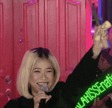 a woman singing into a microphone while wearing a green versace sweatshirt