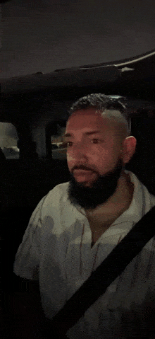 a man with a beard is smiling while sitting in a car at night