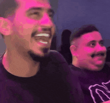two men are sitting next to each other in a dark room and one of them is smiling .