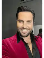 a man with a beard is wearing a red jacket and black shirt