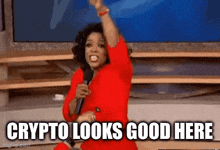 a woman in a red dress is holding a microphone and saying crypto looks good here .