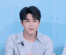 a young man in a blue shirt is sitting in front of a blue wall and making a funny face .