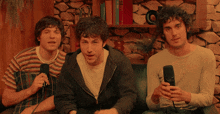 three men are sitting on a couch and one is holding a microphone