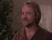 a man with a beard wearing a brown shirt is smiling