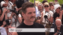 a man with a mustache is standing in front of a crowd with a photocall advertisement on the bottom
