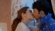a man and a woman are kissing in front of a window in a room .