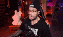 a man wearing glasses and a beanie is screaming into a microphone while sitting in a chair .