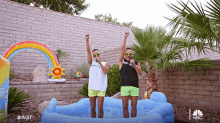 two men singing into microphones in an inflatable pool with a nbc logo in the background