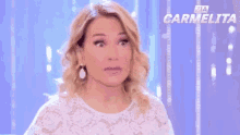 a woman in a white lace top is making a surprised face in front of a banner that says carmelita