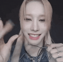 a woman wearing glasses and a necklace is smiling and waving at the camera .