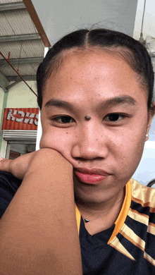 a woman with a black spot on her forehead holds her hand to her face