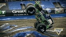 a monster truck is doing a trick on a dirt track in front of an advertisement for monster jam