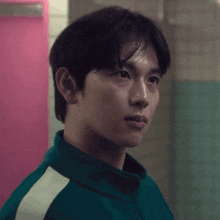 a man in a green jacket stands in front of a pink wall