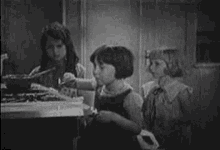 a group of young girls are sitting at a table in a black and white photo .