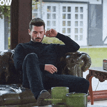 a man is sitting on a couch with his legs crossed and covering his ears with his hand ..