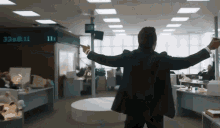 a man in a suit stands in an office with his arms outstretched in front of a digital clock that reads 11:11