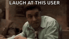 a man in a suit and tie is sitting at a table and laughing at someone .