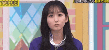 a young woman in a blue jacket is standing in front of a window and making a funny face .
