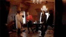 a group of women are dancing in a living room with a chandelier in the background .