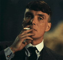 a man wearing a suit and tie is smoking a cigarette