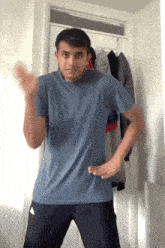 a young man in a blue shirt and black pants is standing in front of a closet .