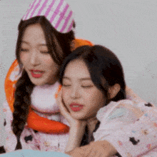 two girls are laying next to each other with their eyes closed and one is wearing a party hat .