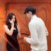 a woman in a black dress and a man in a white sweater are dancing in front of a wooden door