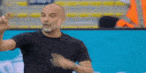 a man in a black t-shirt is standing in front of a blue screen and making a funny face .