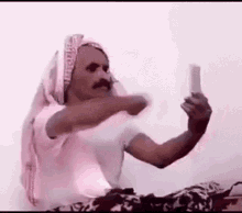 a man in a pink head scarf is taking a selfie with his cell phone .