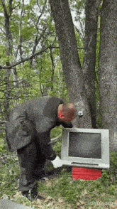 a man in a suit is standing next to a computer monitor in the woods .