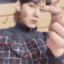 a man in a plaid jacket is making a heart shape with his fingers .