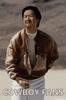 a man in a brown jacket and white pants is standing in the desert .