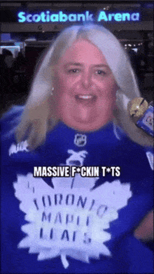 a woman wearing a toronto maple leafs shirt stands in front of the scotiabank arena