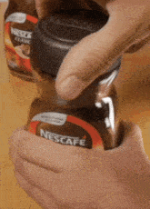 a person is opening a jar of nescafe classic