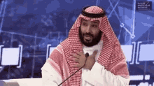 a man in a keffiyeh is talking into a microphone while sitting at a table .
