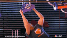 a man is hanging upside down from a rope while wearing an american ninja warrior t-shirt