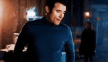 a man in a blue turtleneck is standing in a room .