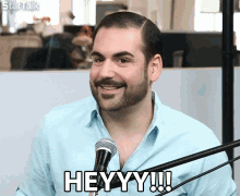 a man with a beard is smiling in front of a microphone and says heyy !!!