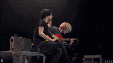 a man with a tattoo on his arm is drinking from a bottle while another man plays a guitar