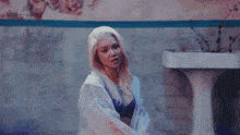 a woman with blonde hair is sitting in front of a bathroom sink .