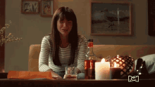 a woman sits on a couch with a bottle of alcohol and a candle in front of her
