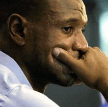 a close up of a man 's face with his hand to his mouth