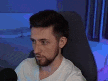 a man with a beard is sitting in a chair and talking into a microphone