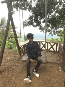 a young man sits on a wooden swing with a view of the ocean