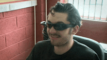 a man wearing sunglasses and a black shirt smiles for the camera