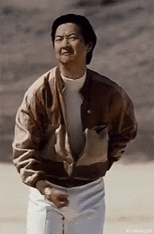 a man wearing a brown jacket and white shorts is standing in the desert .